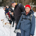 Gruppenbild: Schülerinnen und Schüler auf dem Weg zum Dreisessel. Sie gehen einen schmalen schneebedeckten Pfad entlang. Auch ein kleiner weiß braun gefleckter Hund ist mit dabei.